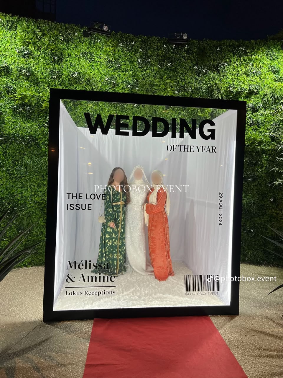 Three guests posing inside a magazine-cover booth against a garden wall